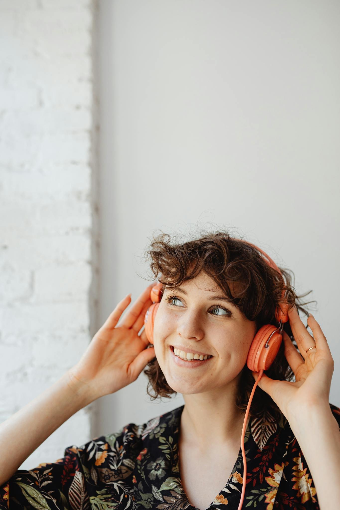 Happy woman with curly hair listens to music using orange headphones against a white background.